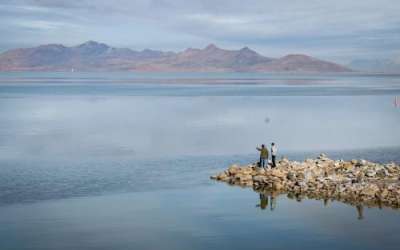 Visitors on Silver Sands Beach at Great Salt Lake State Park, near Magna, stand on rocks jutting out into the iconic saline lake with Antelope Island seen in the background, Jan. 27, 2024. Jim Hill, KUER